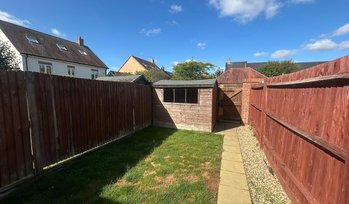 Enclosed rear garden with lawn, paved pathway and brick storage shed